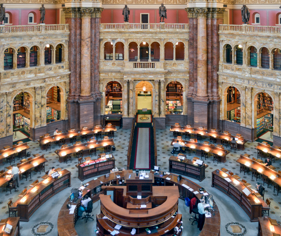 Ornate, multi-level historic library reading room with grand marble columns and extensive bookshelves. Patrons study, research at wooden tables.
